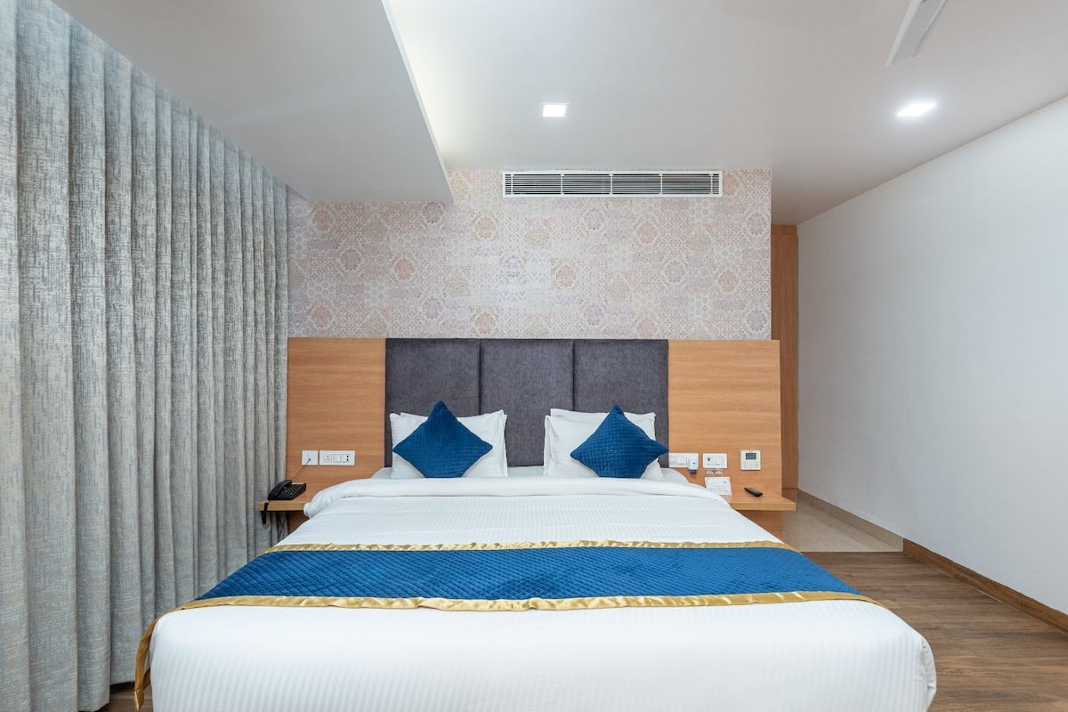 A modern hotel room with a large bed, a headboard with a built-in control panel, and a patterned wall.