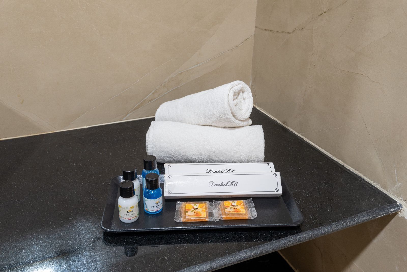 A bathroom counter with a dental kit, two bottles of hair spray, a towel, and a tray of toiletries.