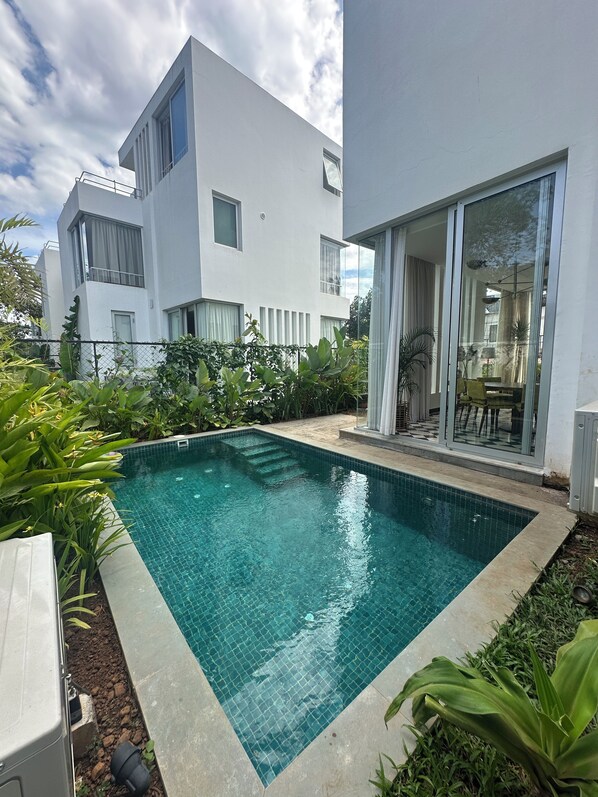 Une maison moderne à deux étages, dotée d’une piscine, entourée d’une végétation luxuriante et d’un jardin bien entretenu.
