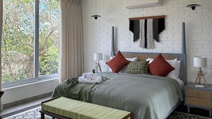 A modern bedroom with a large bed, a bench, a ceiling fan, and a view of trees through the window. - Casa Bella Vita (Anjuna)