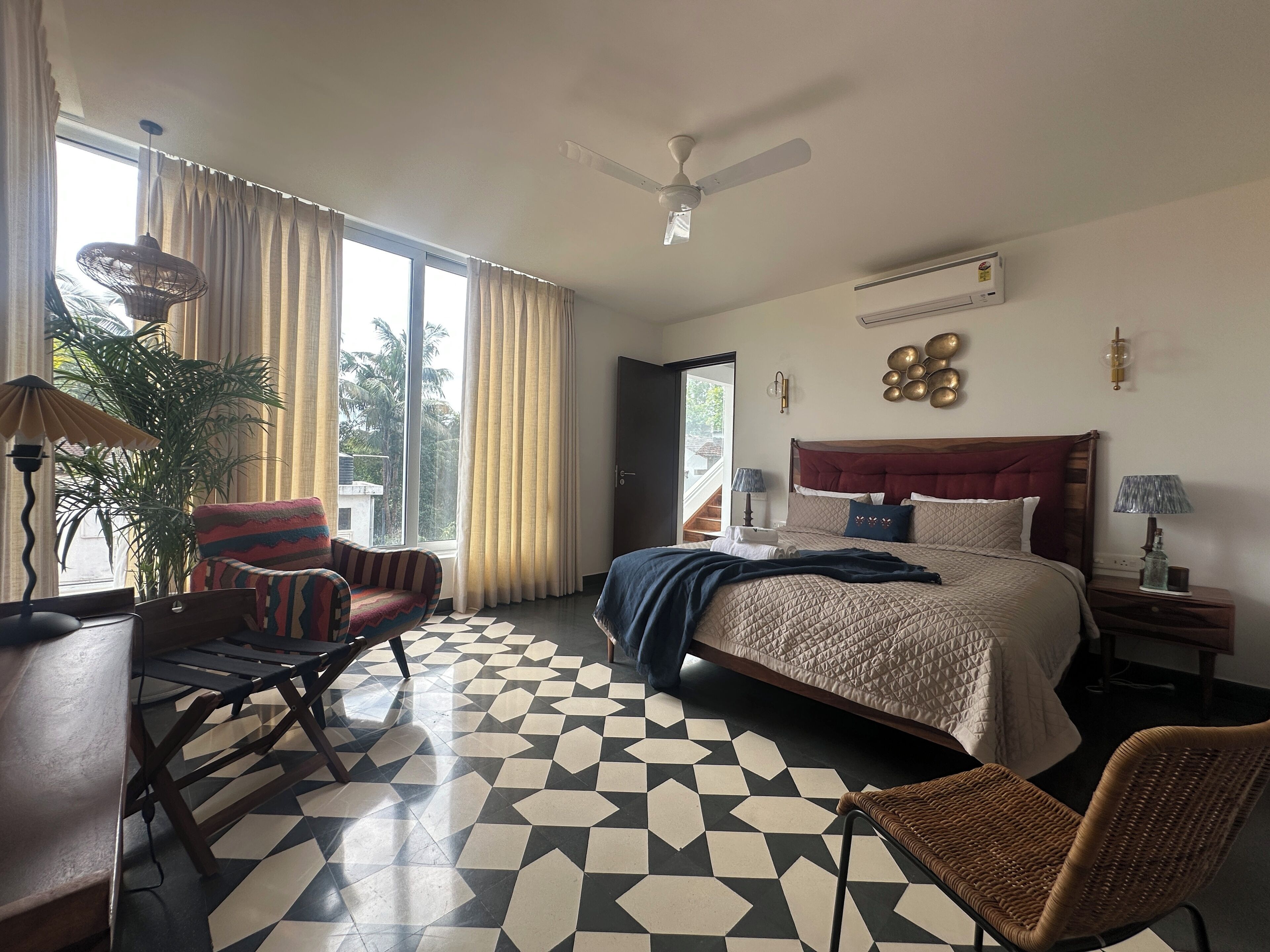 Ein Hotelzimmer mit Bett, Sessel, Schreibtisch, Topfpflanze und Blick ins Freie.