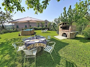 A backyard with a dining table set for four, surrounded by chairs, a barbecue grill, and a pool.