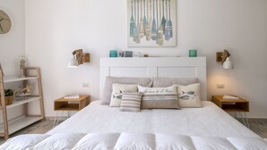 A bedroom with a large bed, two bedside tables, a wall-mounted painting, and a shelf with decorative items.