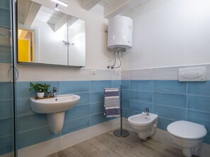 Un bagno con lavandino, bidet e wc, uno specchio e una ventola a soffitto.