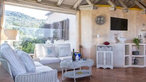 A cozy outdoor seating area with wicker furniture, a small table with a bottle and glasses, and a decorative cabinet with shelves. - Beautiful private villa with WIFI, A/C, private pool, TV, patio, pets allowed and panoramic view (Olbia)