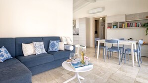 A modern living room with a blue sofa, a dining area with blue chairs, and a kitchen in the background. - Beautiful private villa for 7 guests with private pool, A/C, WIFI, TV and patio (Budoni)