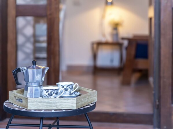 A coffee setup with a French press, cups, and saucer on a wooden tray on a round table.