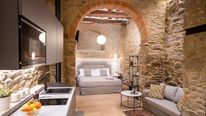 Une cuisine moderne dotée d’un four encastré et d’un bar pour prendre le petit-déjeuner, une chambre confortable avec un grand lit et une table de chevet, et un espace de vie comprenant un canapé et une table basse.