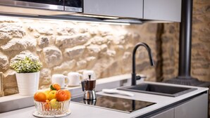 Une cuisine avec un mur en pierre, un évier, une machine à café et un panier de fruits posé sur le comptoir.