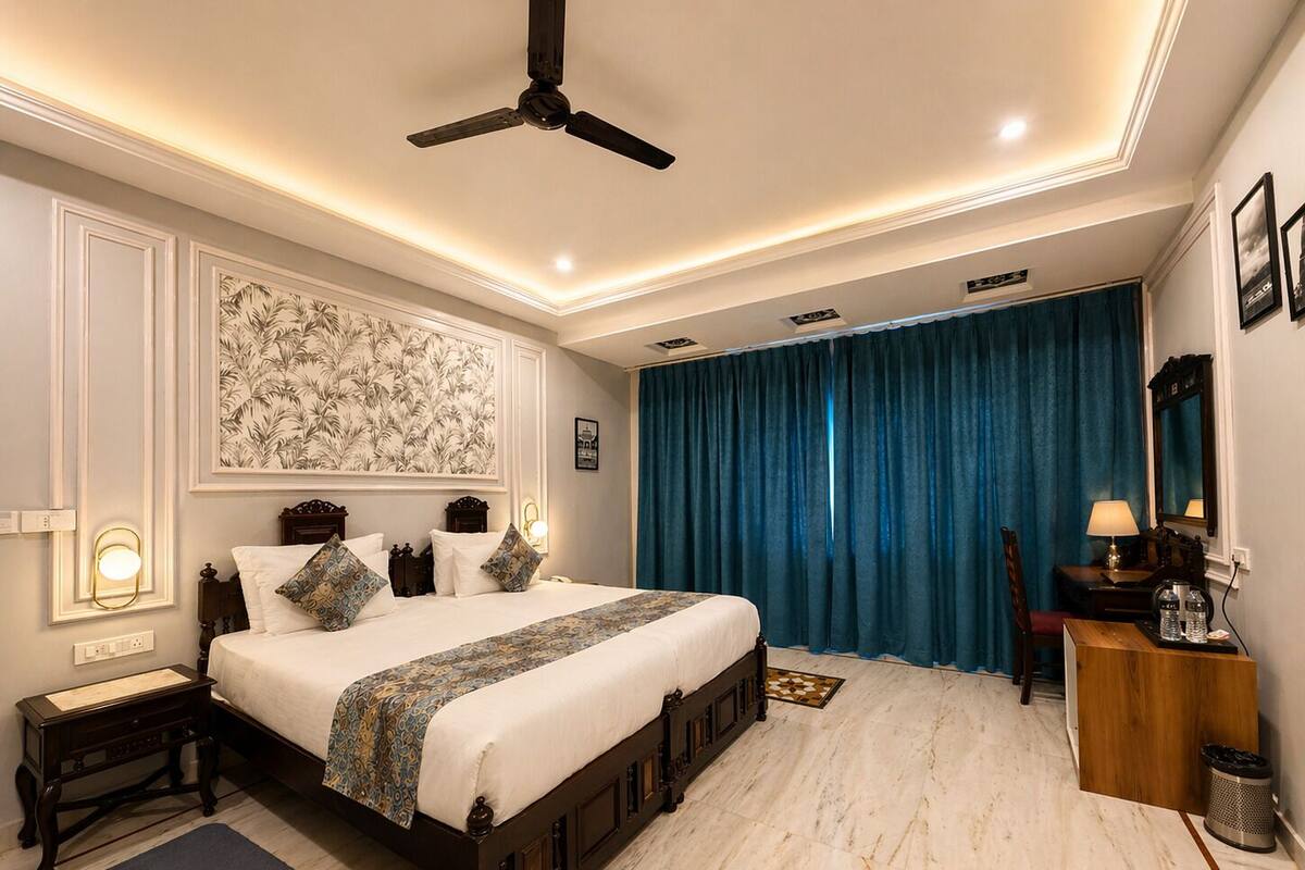 A bedroom with a large bed, a ceiling fan, a nightstand, a desk, a chair, and a large window with blue curtains.