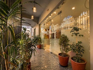 Un couloir agrémenté de plantes en pot, un mur de verre orné d’un motif décoratif et des lampes suspendues.