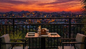 A dining table with chairs and a view of a cityscape at sunset. - The Crescent Udaipur | Boutique Hotel Near Lake Pichola (Udaipur)