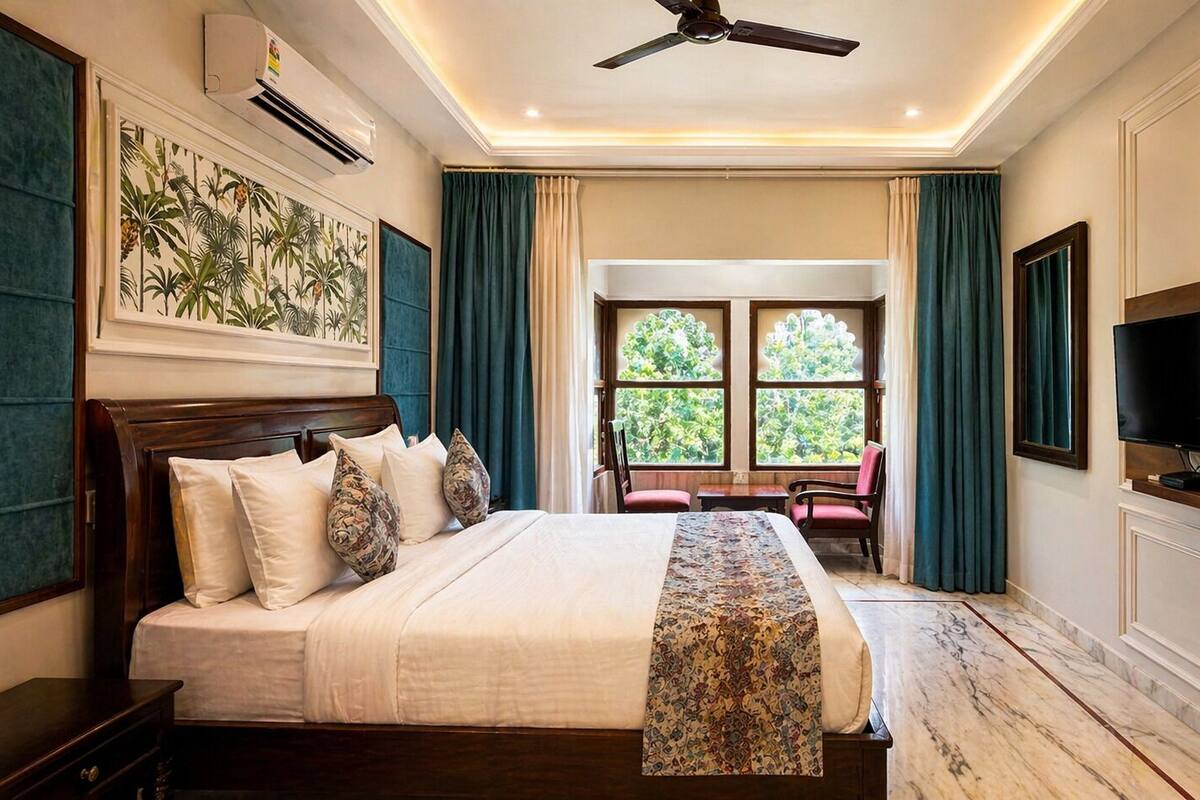 A hotel room with a large bed, a TV, a ceiling fan, and a window with a view of greenery.