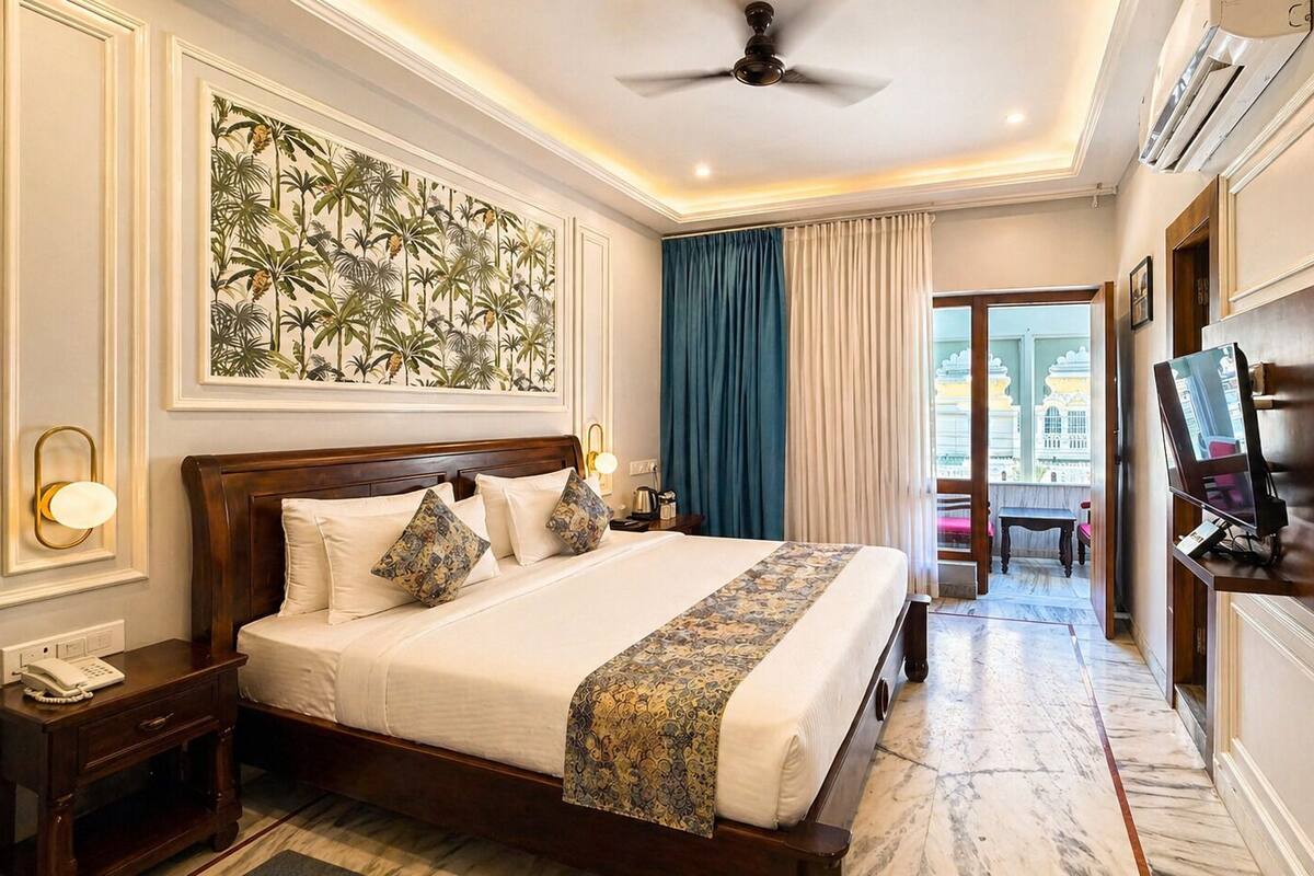 A hotel room with a large bed, a television, a desk with a telephone, a wall-mounted air conditioner, and a balcony with a view.