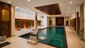 A modern indoor pool area with a glass ceiling, wooden paneling, and a clear view of the sky. - The Crescent Udaipur | Boutique Hotel Near Lake Pichola (Udaipur)