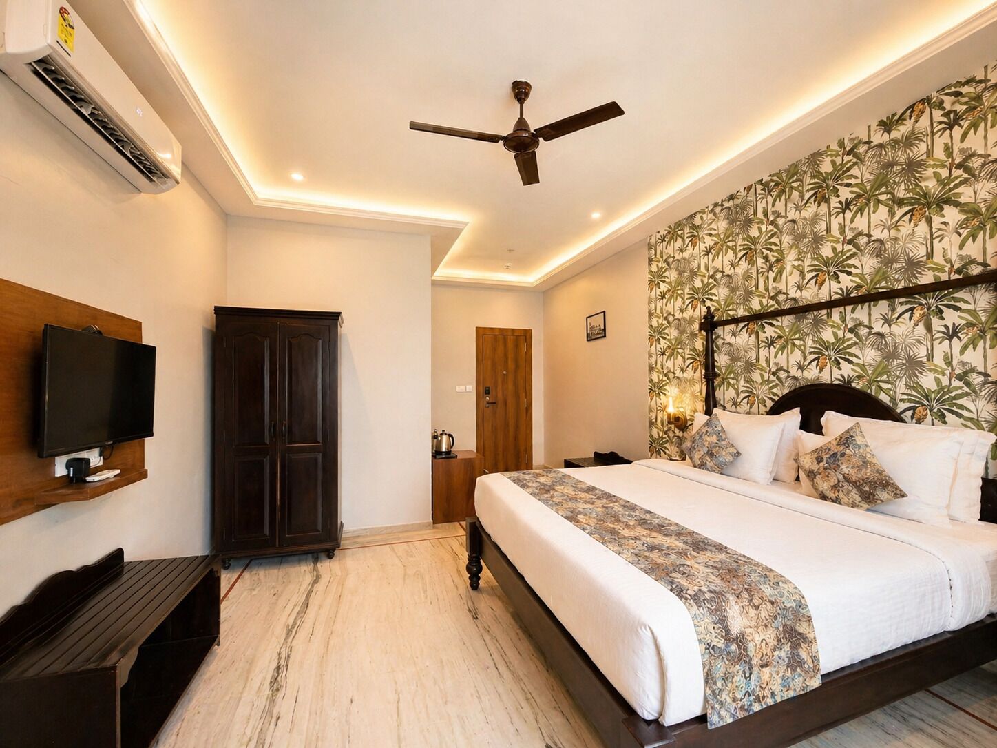 Un dormitorio con una cama, televisor, ventilador de techo y una pared con papel tapiz tropical.