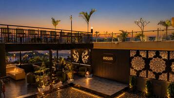 Um bar no terraço com vista para a cidade, mesas ao ar livre e painéis decorativos na parede.