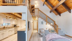 Un vaste espace de vie avec un escalier, une cuisine dotée de meubles blancs et un coin salon confortable agrémenté d’une couverture.