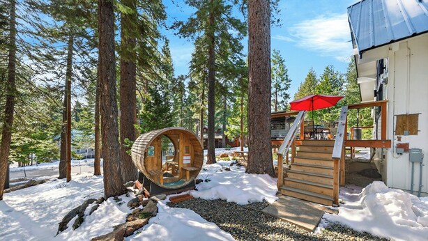 Une cabane en bois, surmontée d’un parasol rouge, entourée de grands arbres et de neige.