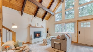 Un salon chaleureux avec une cheminée, des poutres en bois et de grandes fenêtres.