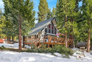 Una cabaña con terraza de madera, rodeada de árboles y nieve.