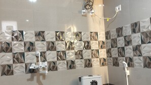 A modern bathroom with a toilet, a shower unit, and a water heater mounted on the wall. - Xact Homes  (Noida)