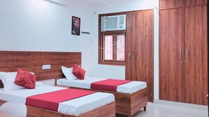 A hotel room with two wooden beds, a wardrobe, a ceiling fan, and a window with an air conditioner. - Xact Homes  (Noida)