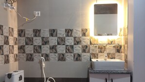 A bathroom with a toilet, bidet, and sink, featuring geometric patterned tiles and a wall-mounted mirror. - Xact Homes  (Noida)