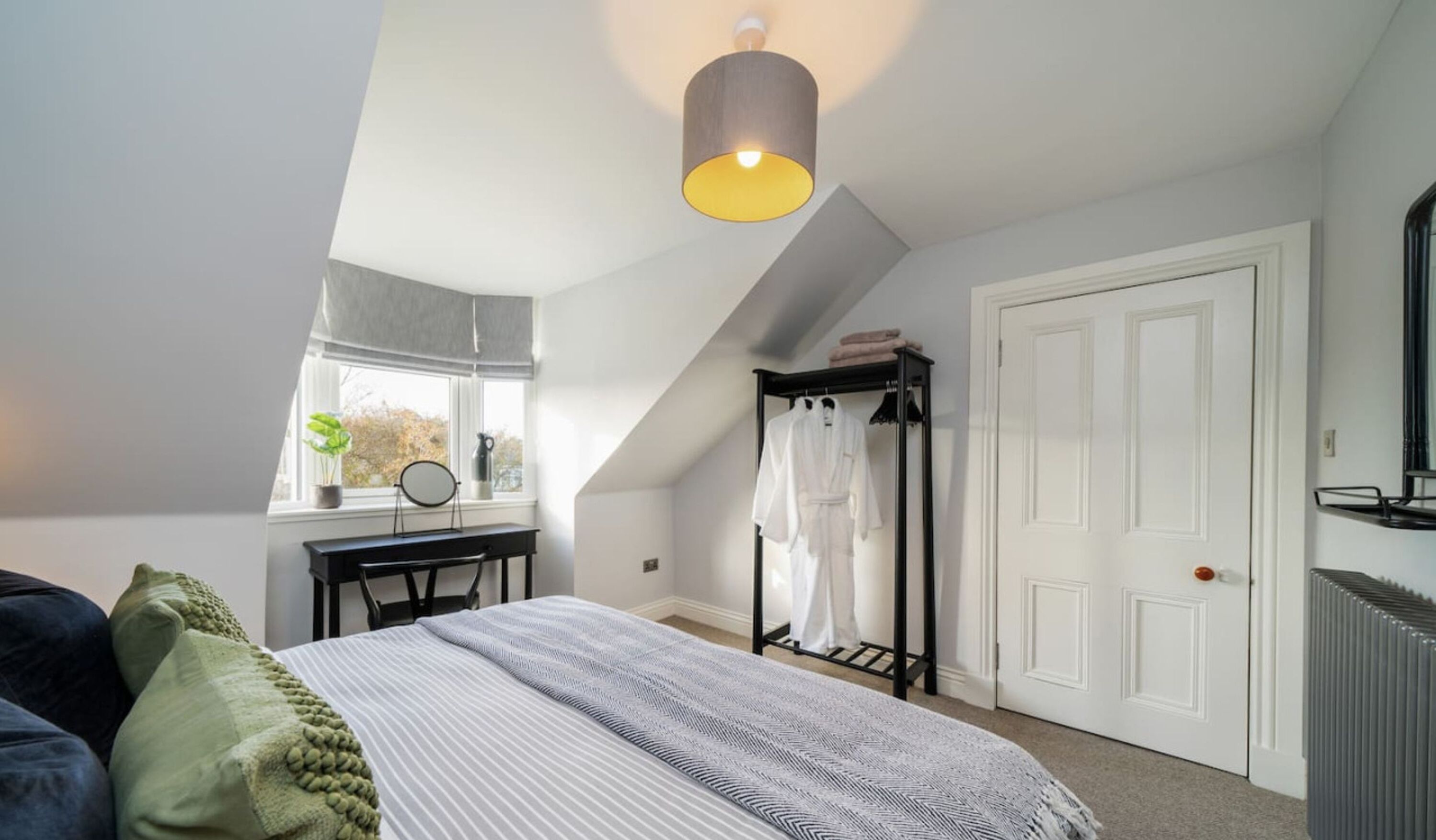 A bedroom with a bed, a desk, a chair, a radiator, and a window with a view of trees.