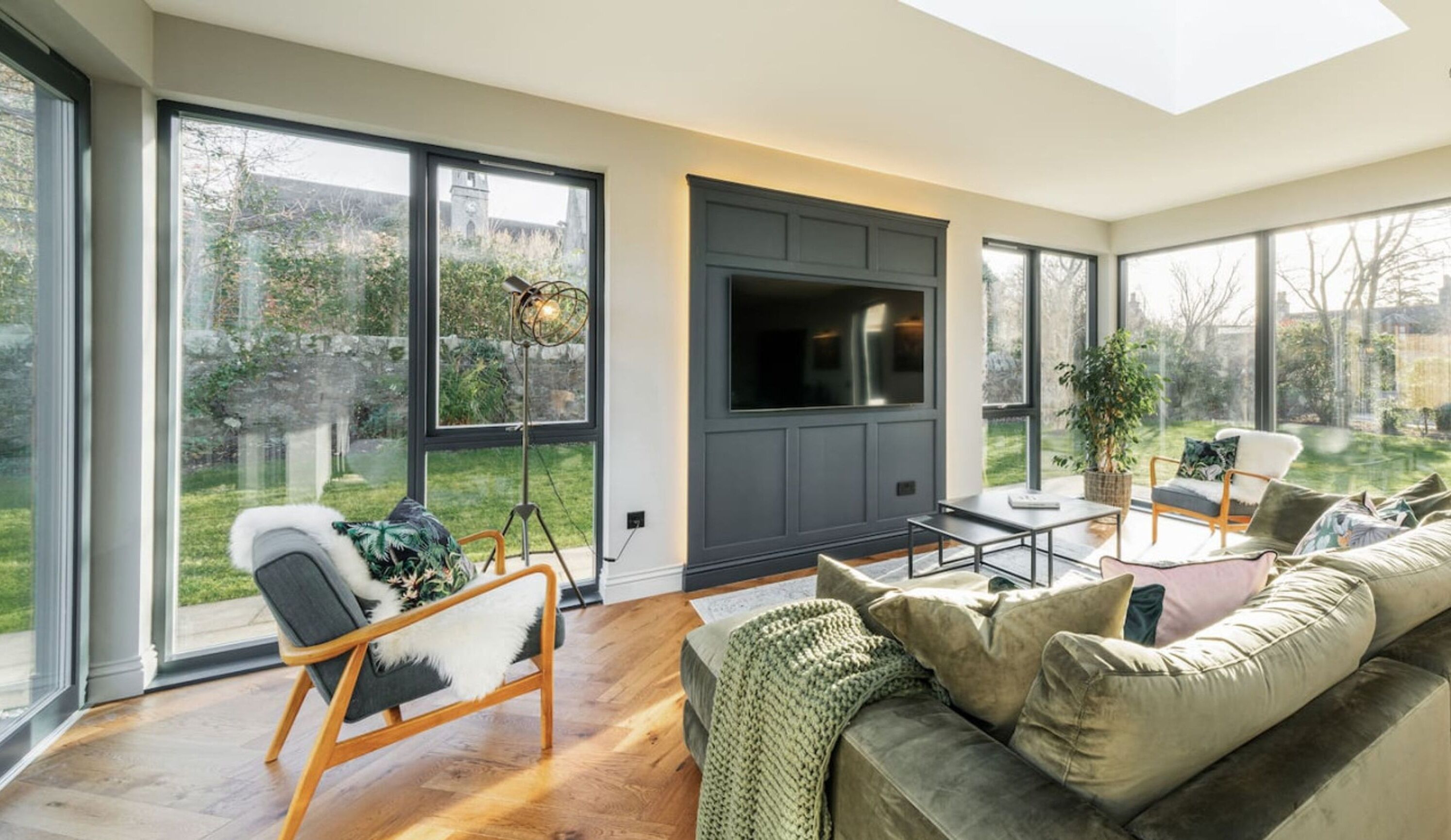 A modern living room with large windows, a flat-screen TV, a sofa, and a coffee table.