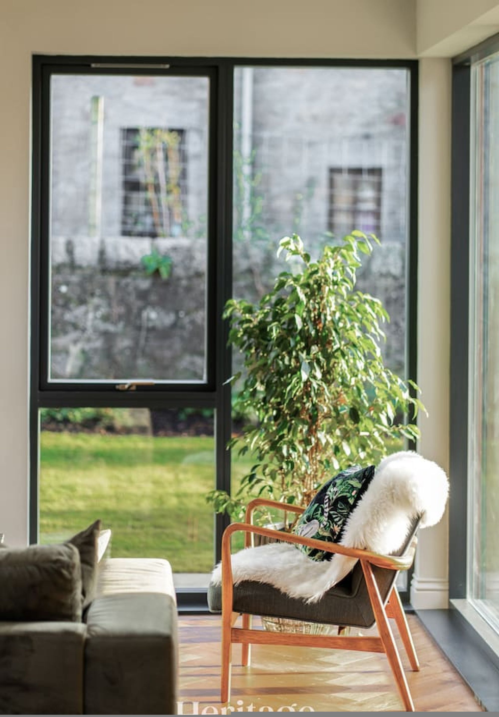 Un salon moderne avec une grande fenêtre, un canapé et un fauteuil agrémenté d’une plante.
