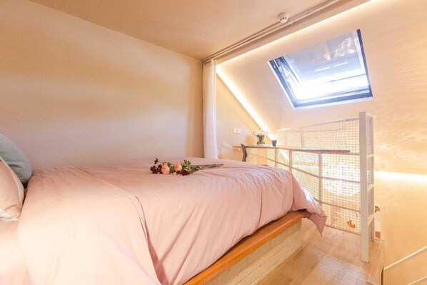 A bedroom with a bed, a skylight, a small table, and a chair.