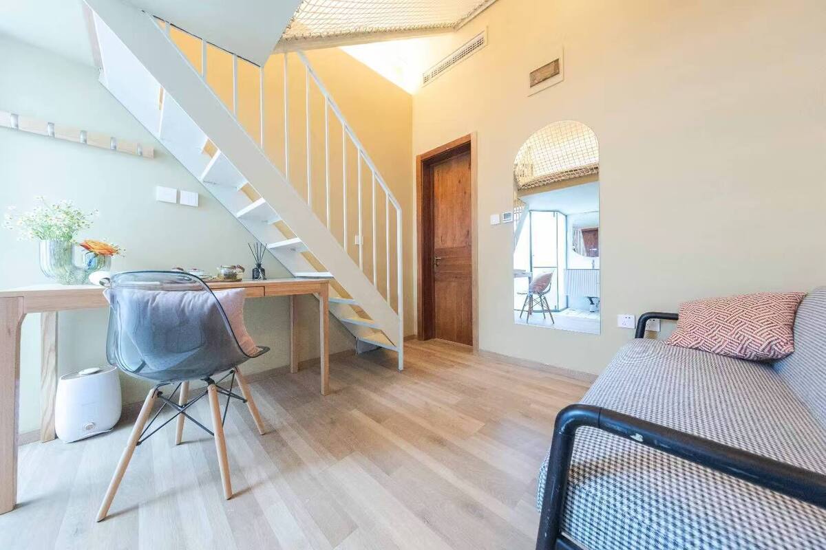 Un intérieur moderne comprenant un bureau en bois, une chaise, un canapé, un escalier et une porte donnant sur une autre pièce.