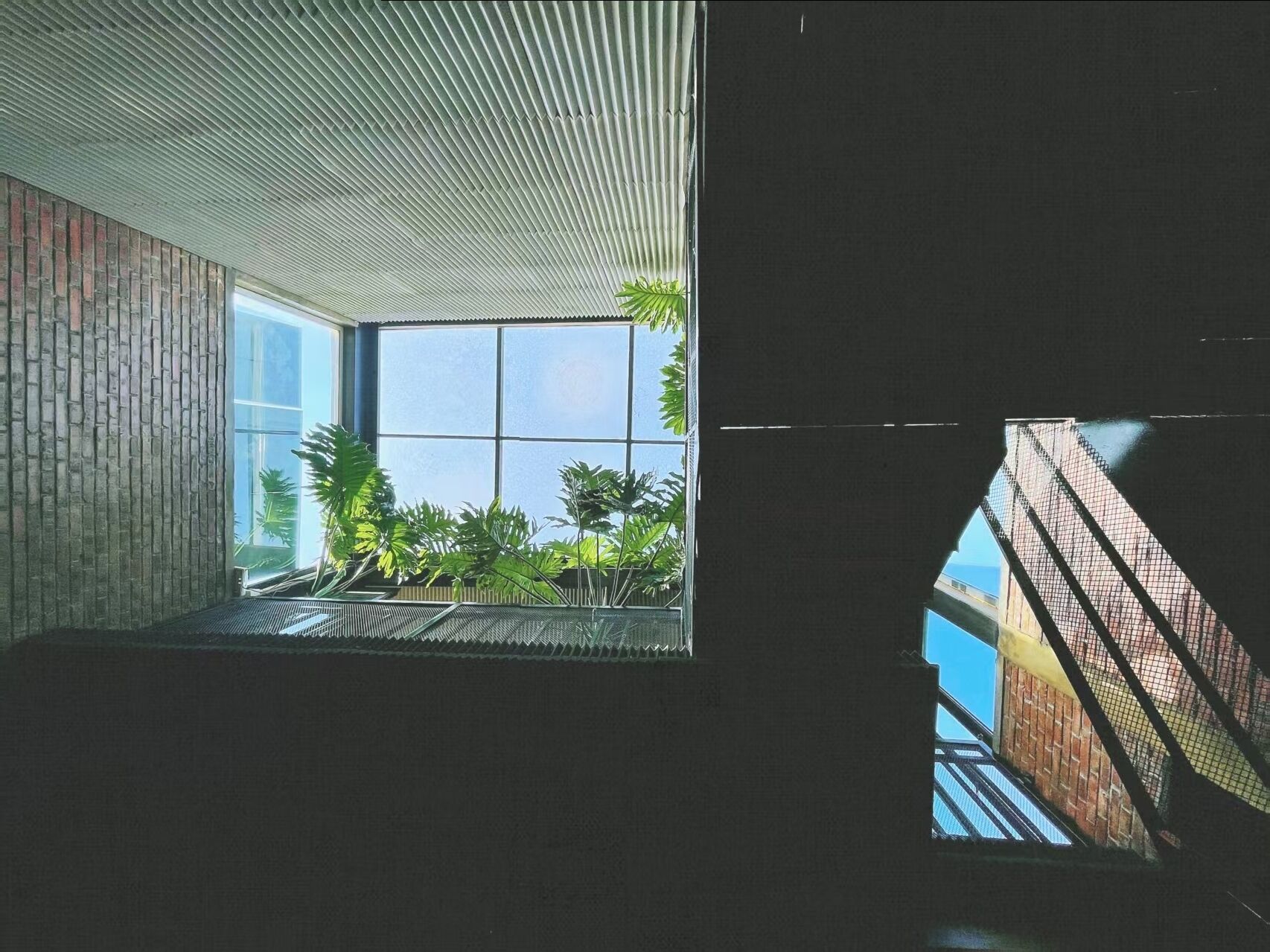 A narrow corridor with a skylight leading to a brick floor and a glass wall.