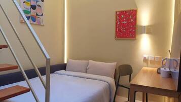 Un dormitorio con cama, escritorio, silla, escalera y dos obras de arte en la pared.