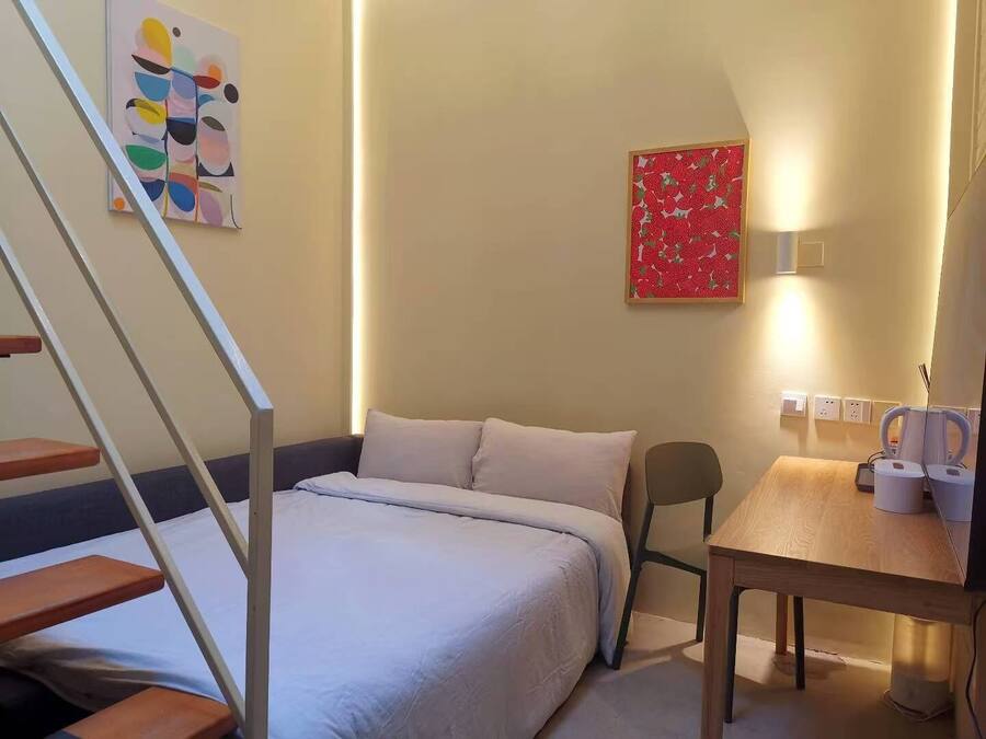 Un dormitorio con cama, escritorio, silla, escalera y dos obras de arte en la pared.
