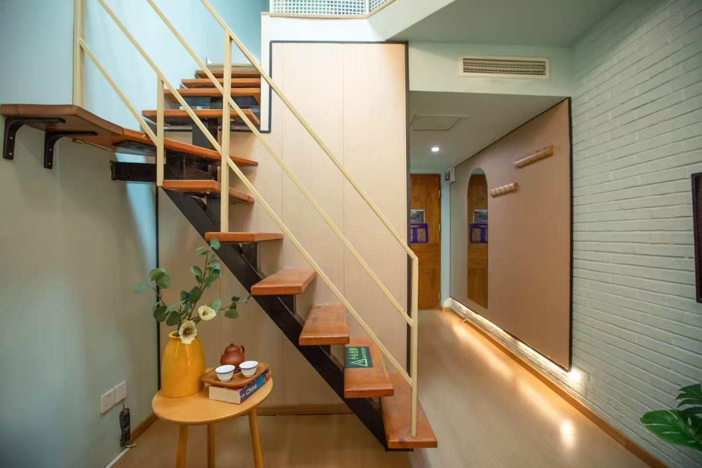 Un escalier avec des marches en bois et une rampe noire, menant à un palier avec un mur blanc et une porte.