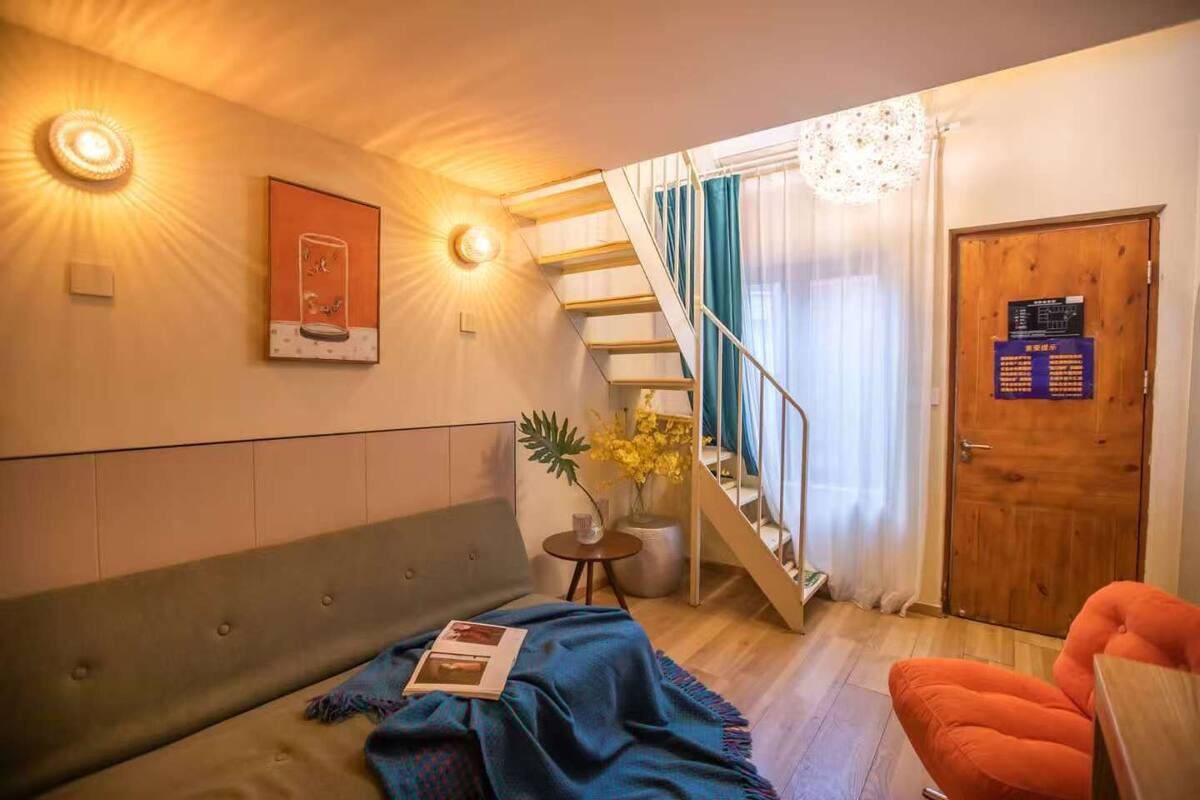 Un salon chaleureux avec un canapé, une petite table sur laquelle est posé un vase de fleurs, un escalier et une porte avec une pancarte.