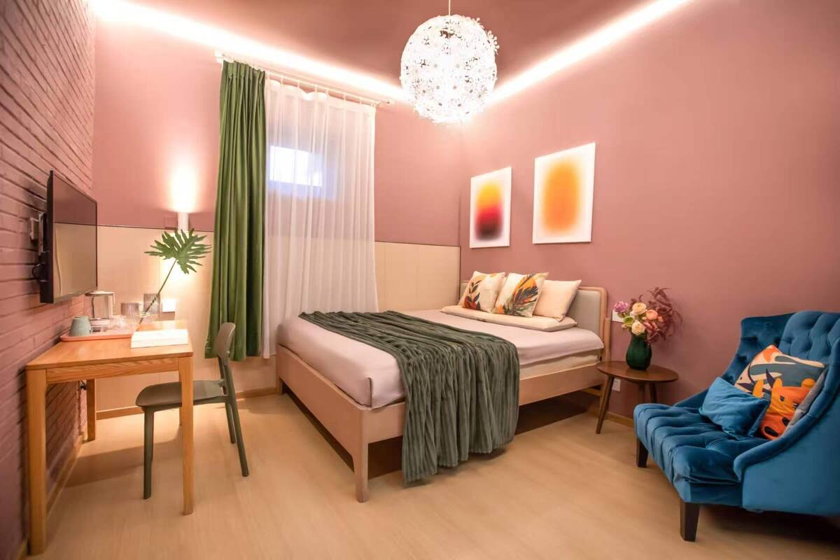 Une chambre d’hôtel moderne, équipée d’un lit, d’un bureau, d’une chaise, d’un canapé bleu et d’une plante décorative.