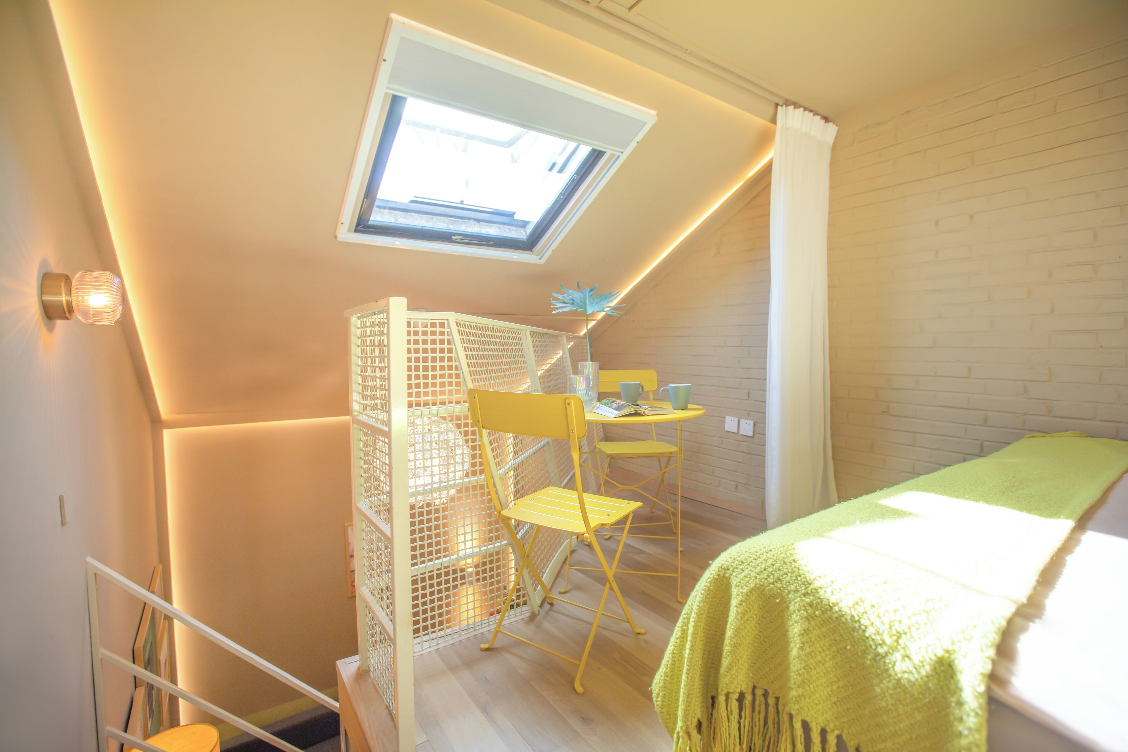 A compact room with a skylight, a bed, a desk with a chair, and a small table.