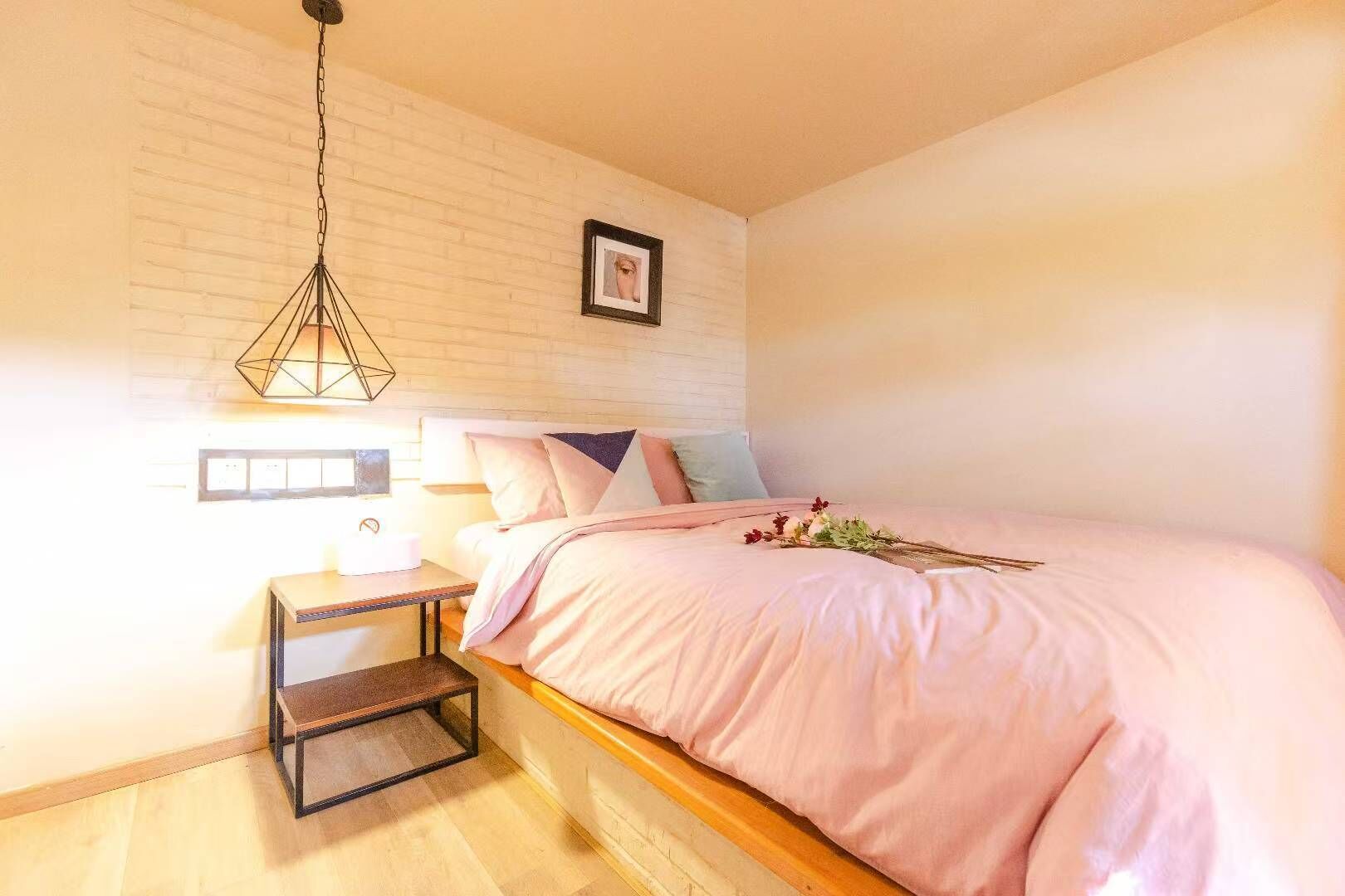 A bedroom with a bed, bedside table, lamp, and a picture on the wall.