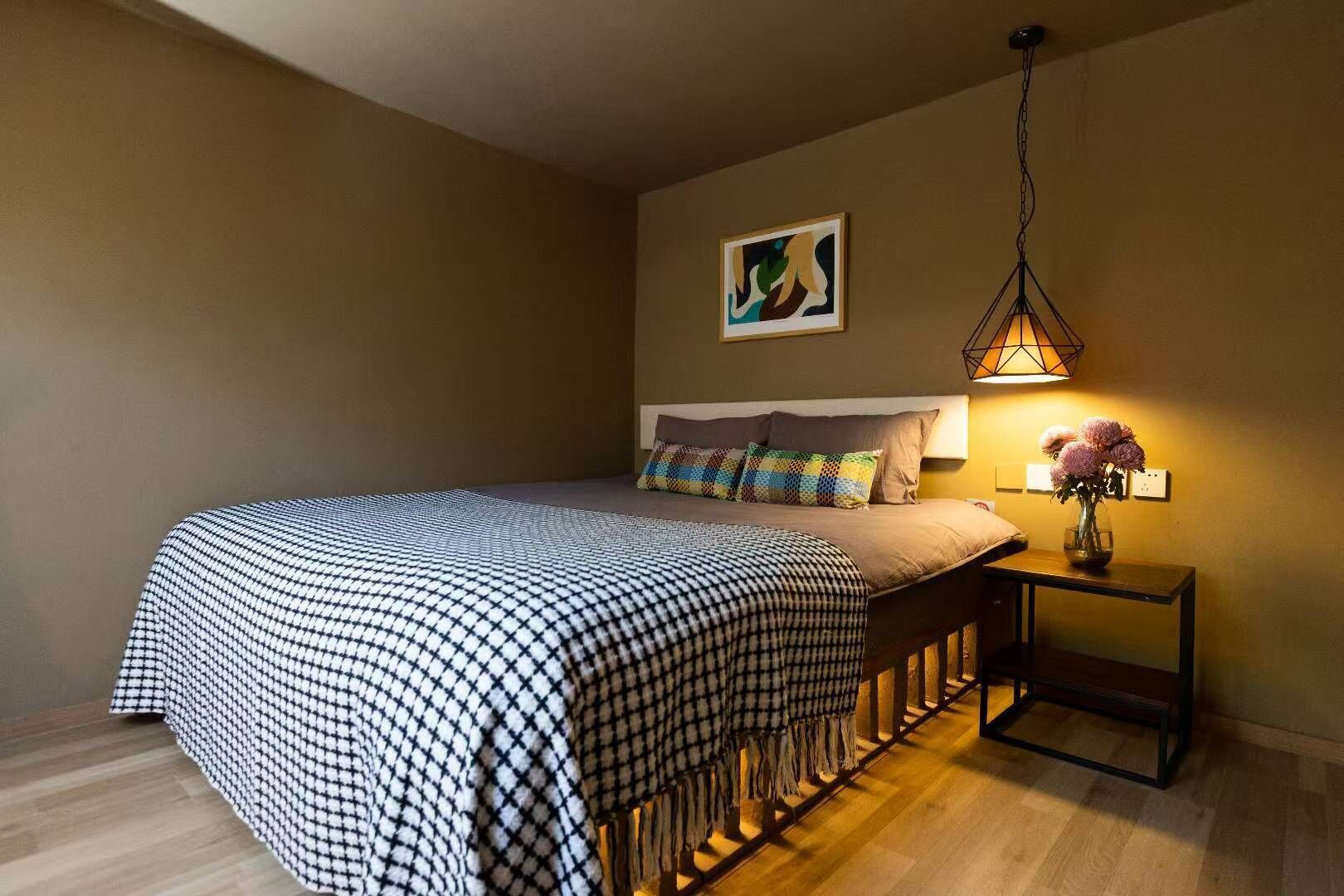 Un dormitorio con una colcha a cuadros, una mesita de noche con una lámpara y un cuadro en la pared.