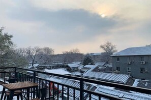 A view of a residential area with snow-covered rooftops and buildings, a wooden deck with chairs, and a cloudy sky. - Beijing Drum Tower Loft Courtyard Hotel (Beijing)