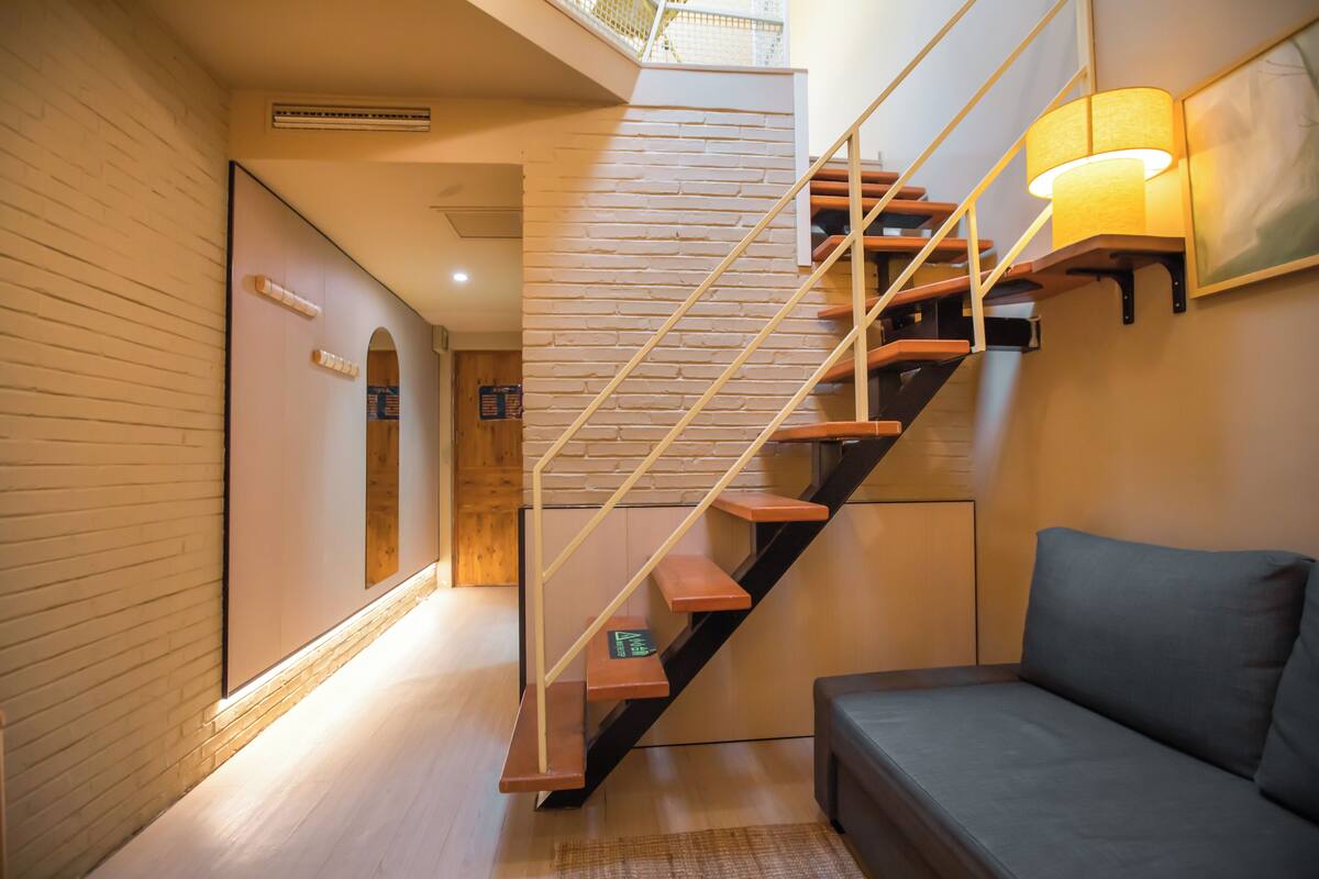 Un intérieur moderne avec un escalier, un canapé et une lampe fixée au mur.