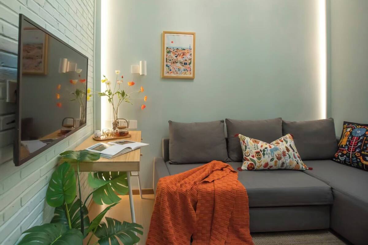 Un salon moderne avec un canapé gris, une table d’appoint en bois et une grande plante.