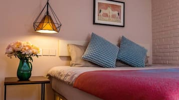 A bedroom with a bed, pillows, a vase with flowers, a hanging light fixture, and a framed picture on the wall.
