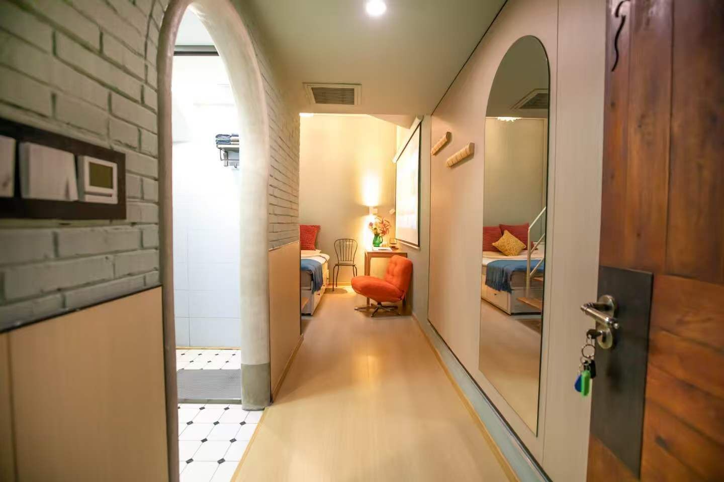 A narrow hallway leading to a bedroom with a bed, a chair, and a desk.