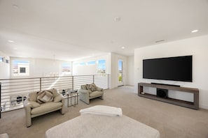 A spacious living area with a large flat-screen TV, two sofas, a coffee table, and a balcony with a railing.