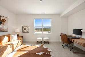 A modern living room with a leather sofa, a desk with a computer, and a large window with a view. - Palladium Palace: Pool+Spa, EV Charger, Miralon! (Palm Springs)