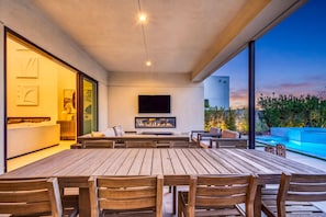 A modern outdoor living space with a dining area, seating, and a flat-screen TV.